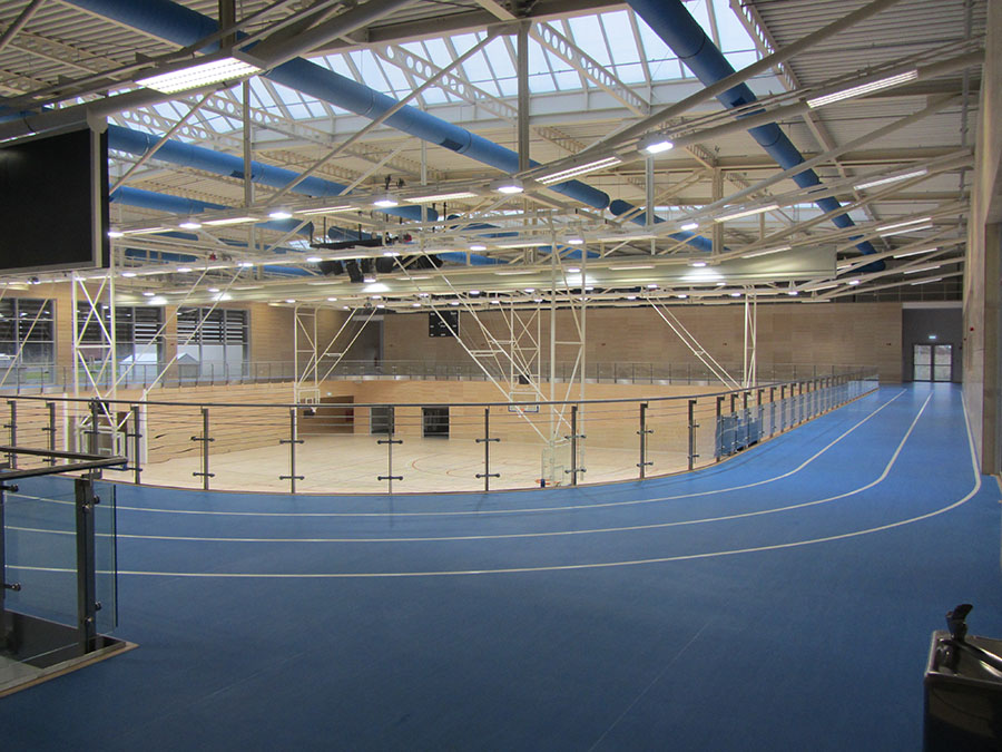 Sporthalle mit hellem Boden und blauer Rundlaufbahn im 1. OG